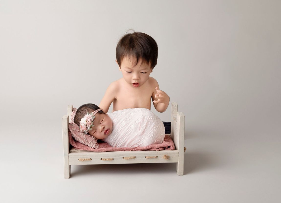 Toddler boy looking at newborn sister in teeny bed.