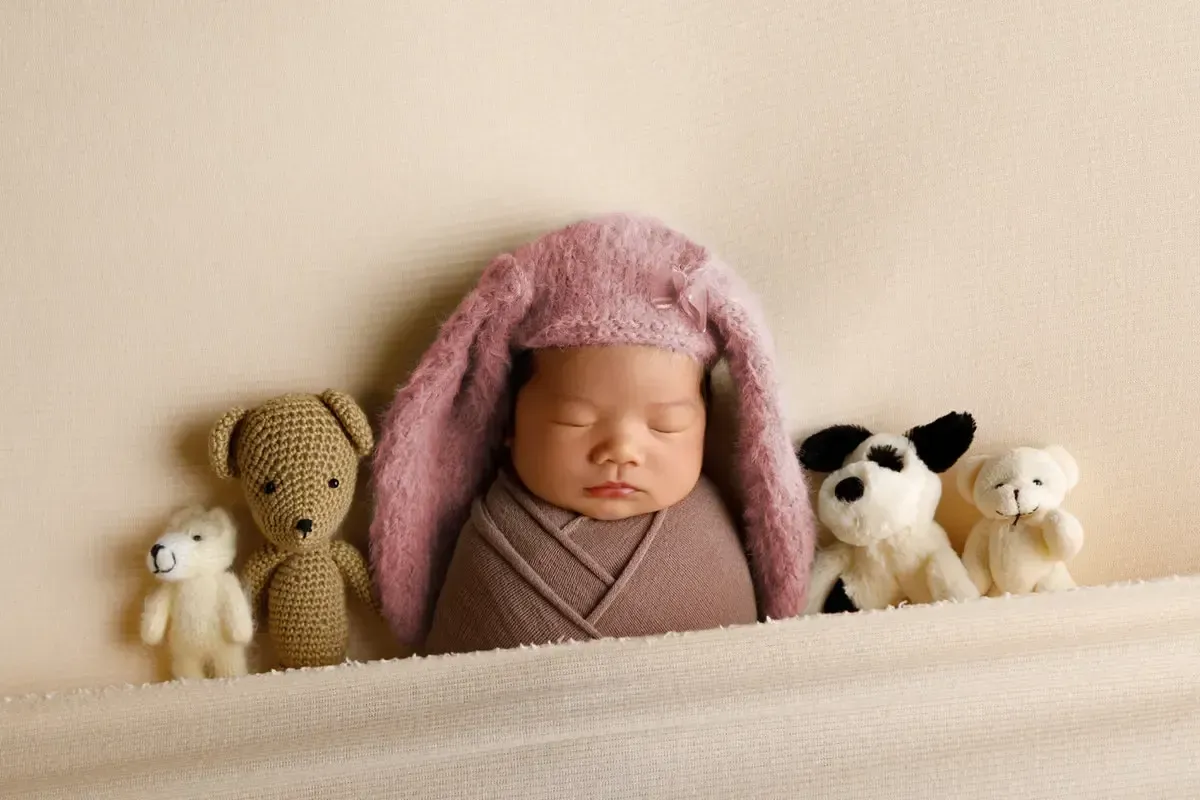 Newborn girl in rabbit ear cap tucked in bed with lovies