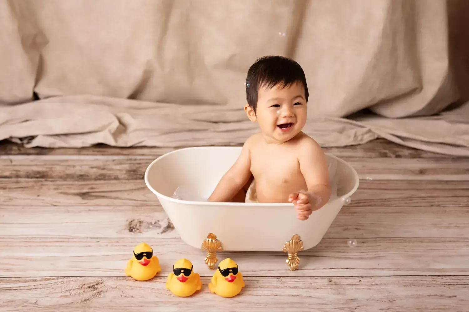 Asian 9 month old boy sitting in bathtub laughinh. Bubbles. Rubber Duckie