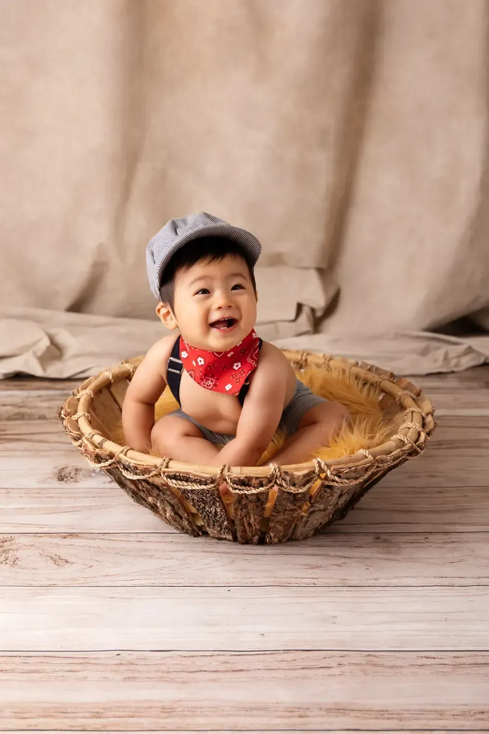 9 month old boy sitting in wood bowl in railroad engineer outfit.