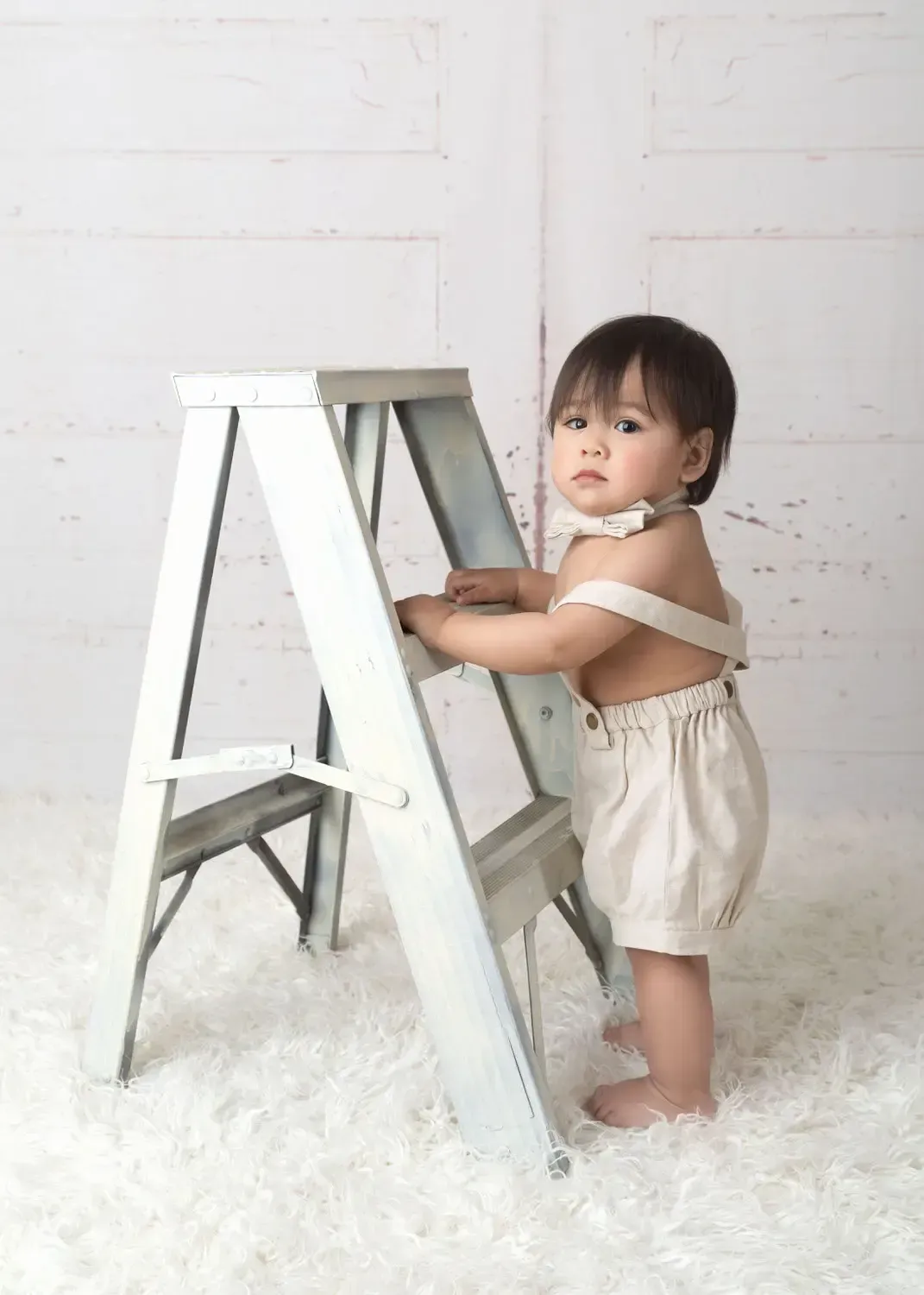 Baby boy first year portraitl . Cream overall shorts on ladder