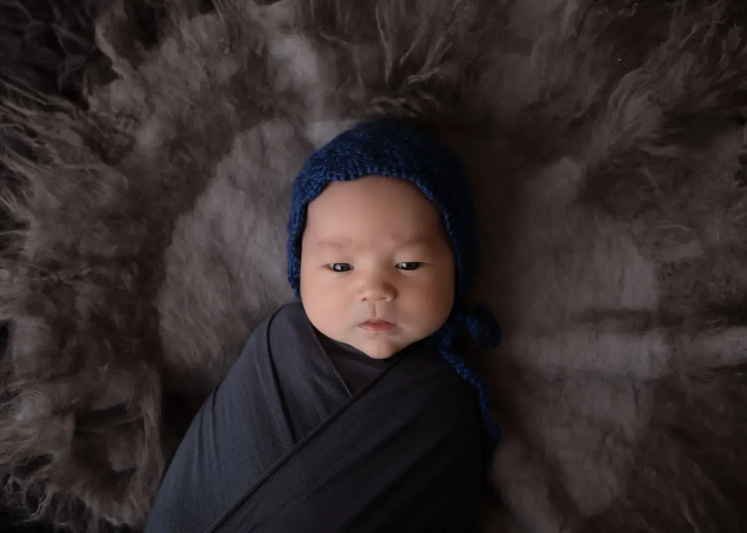 Newborn boy on grey in blue bonnet
