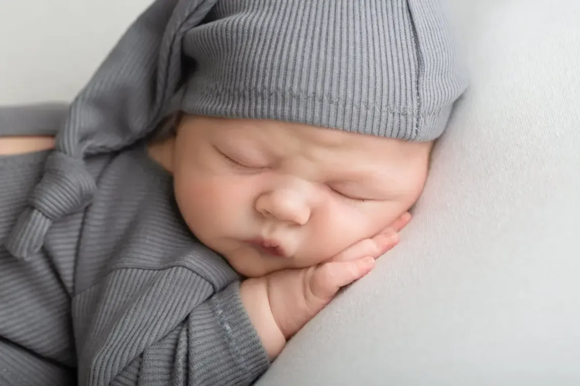 Newborn boy in grey romper. Sleeping on hand with sleepy hat.