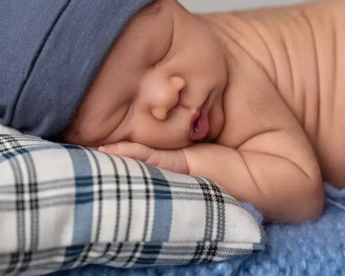 Newborn Boy close up of face on plaid pillow wearing sleepy hat.