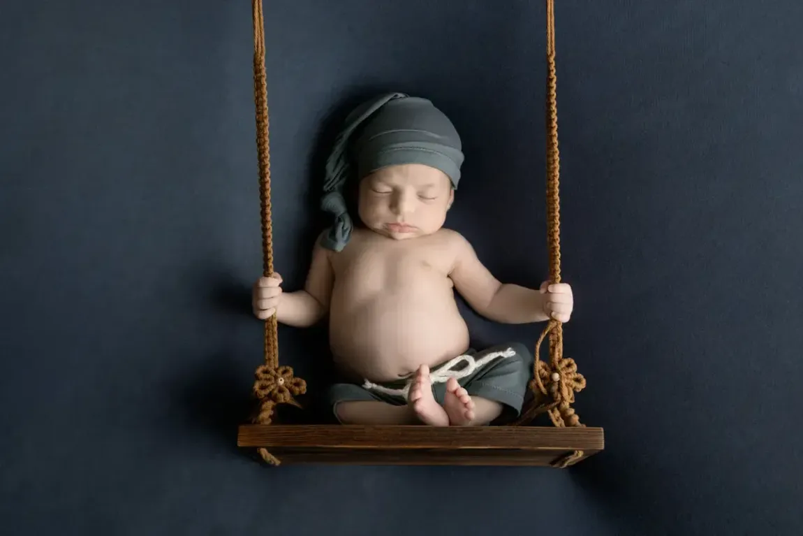 Newborn boy in sleepy hat and short PJs on swing.