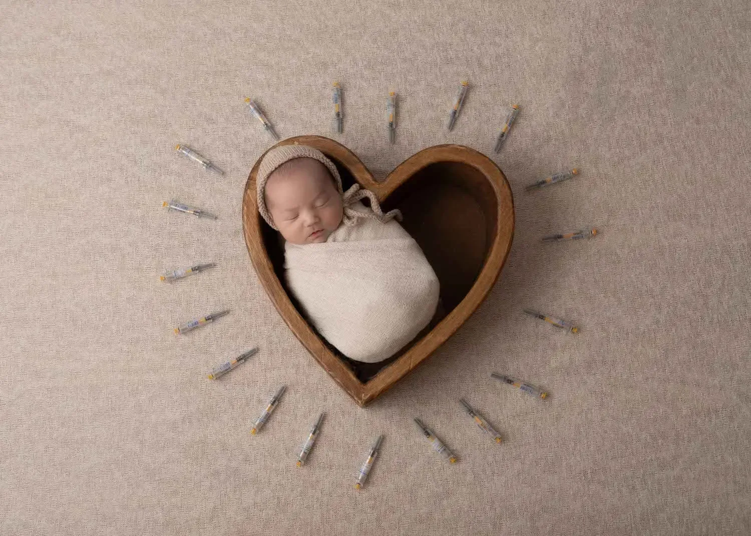 Newborn boy in heart prop flanked by ivf needles