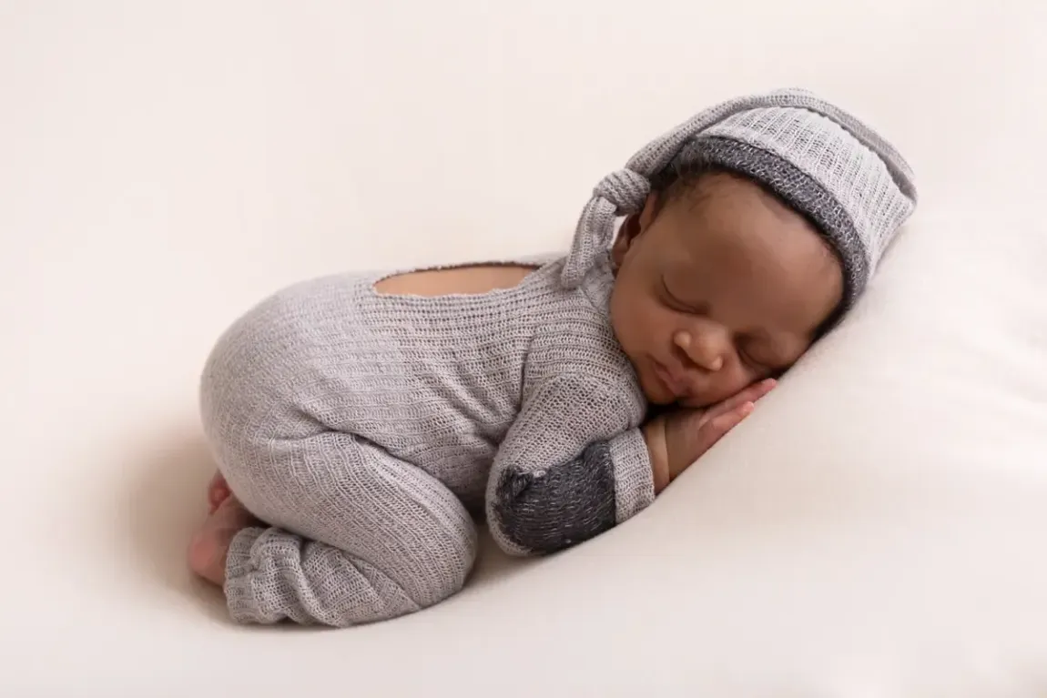 Newborn boy in grey romper with matching sleeping had. On tummy.