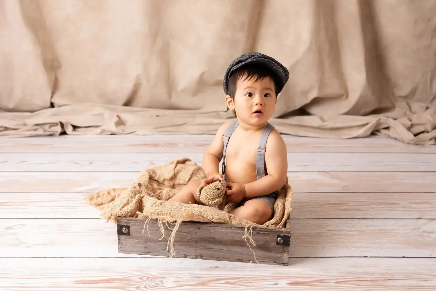 Asian baby boy 9 months old sitting in vintage postal box wear a newsboy hat, grey shorts and suspenders.