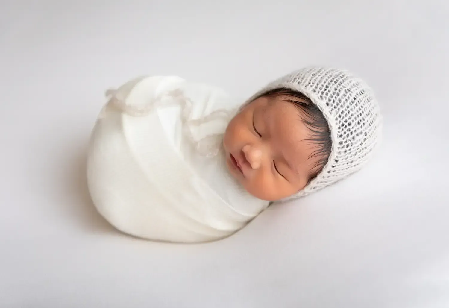 Newborn boy wrapped in white with matching bonnet