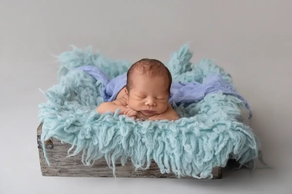 Newborn boy chin on hands in wooden box. 