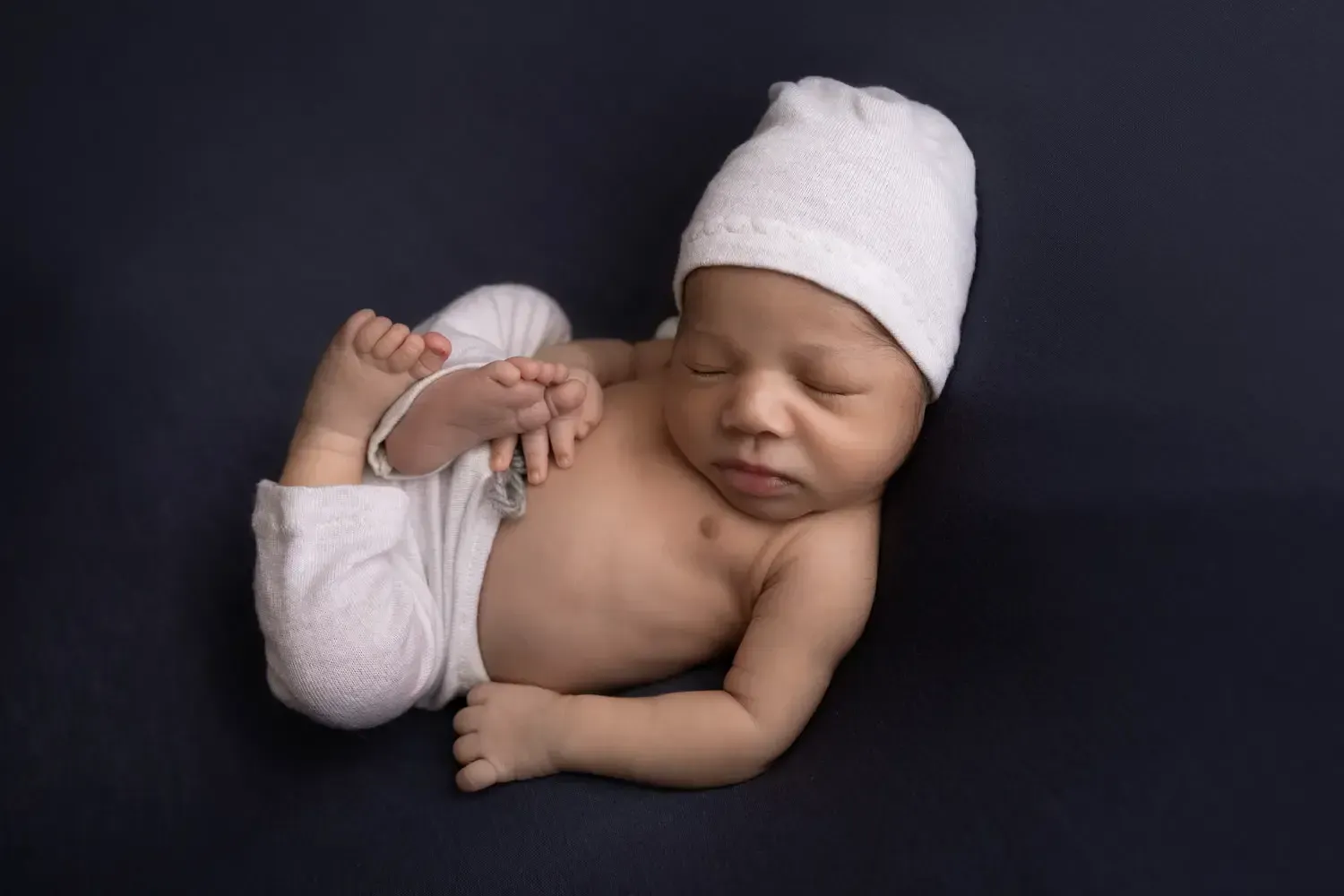 Newborn boy in white shorts and matching sleepy hat. Huck Finn pose.
