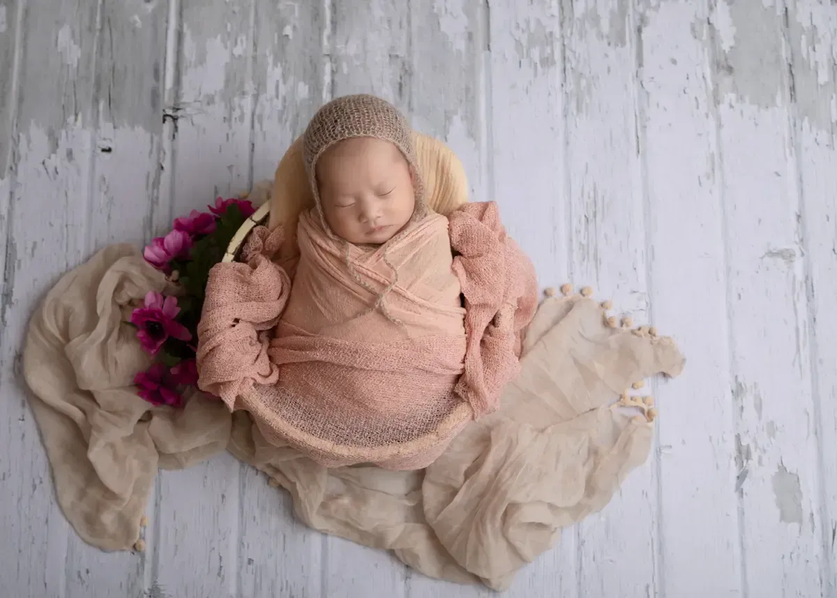 Newborn girl in pink woolen knitted bonnet wrapped and placed in bucket.