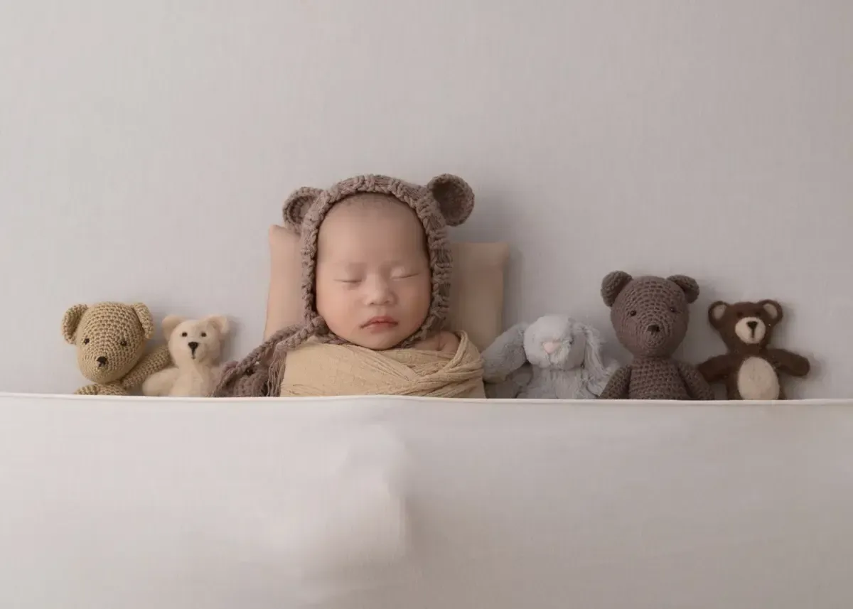 Newborn girl in teddy near hat tucked in with stuffies.
