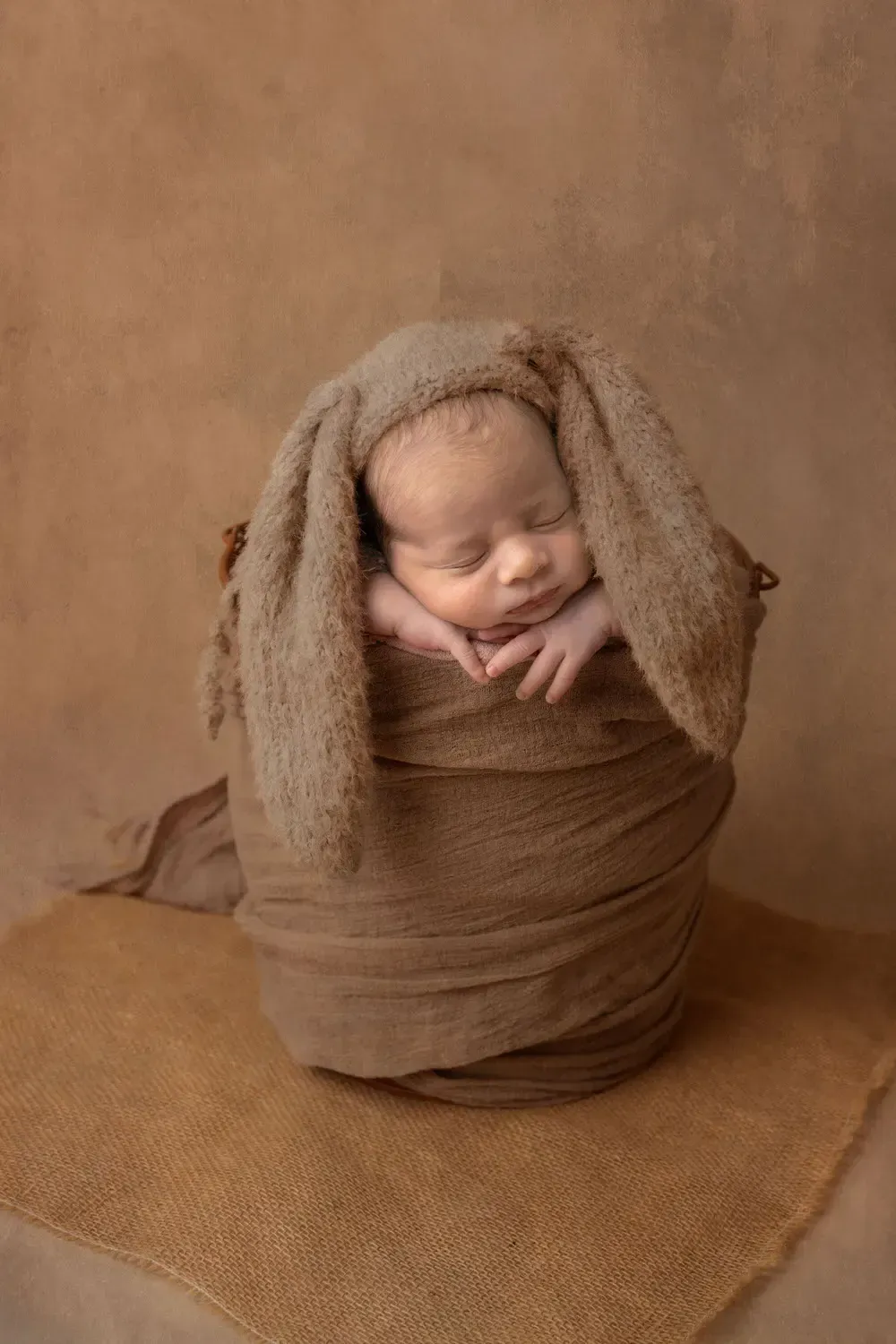 Newborn boy in bucket. Chin on hands. Rabbit ears bonnet.