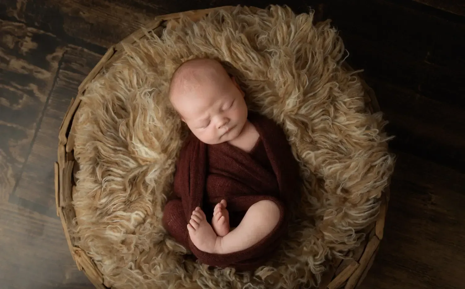Newborn boy wrapped with legs showing in wooden nest.