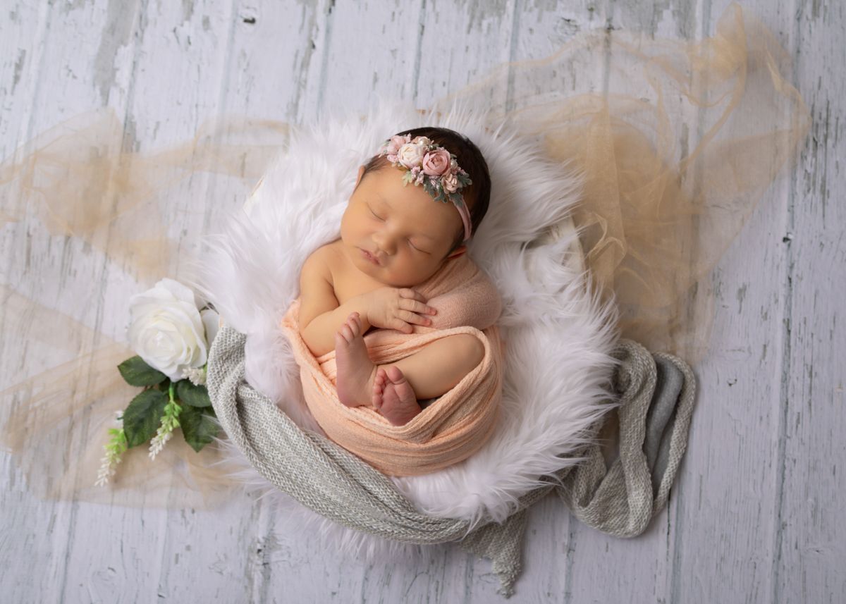 Newborn girl wrapped in peach colored wrap with toes and fingers showing. Newborn Photo Shoot.