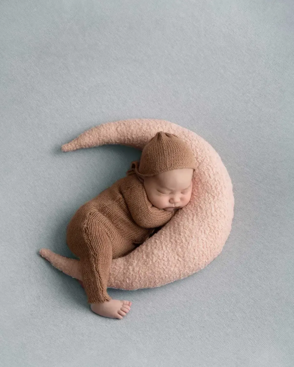 Newborn boy in brown knitted romper and hat on moon pillow