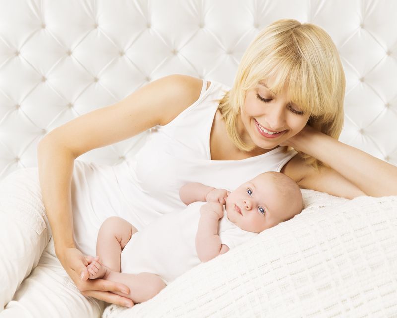 Mom with baby in white lying on a bed
