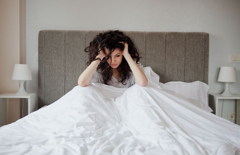 A young woman under the covers feeling stressed and sad.