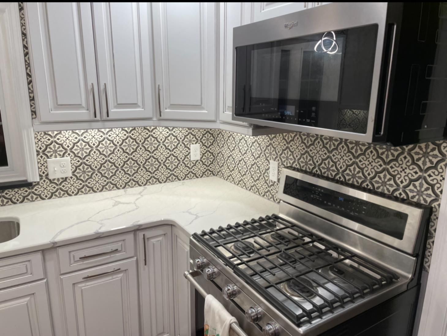 Person in gloves placing tile on a mortar bed with level and mallet nearby.