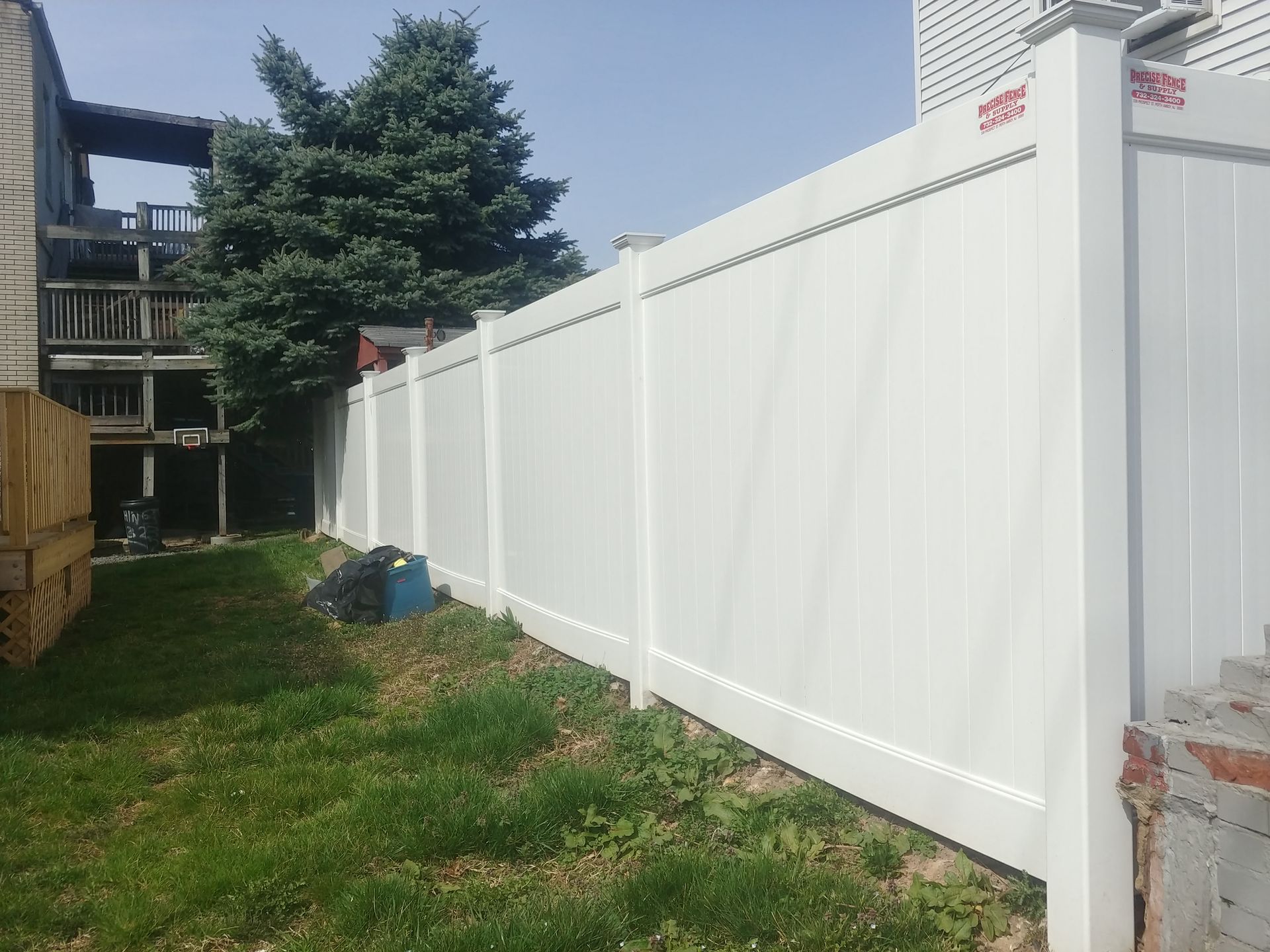A white fence surrounds a grassy yard in front of a house.