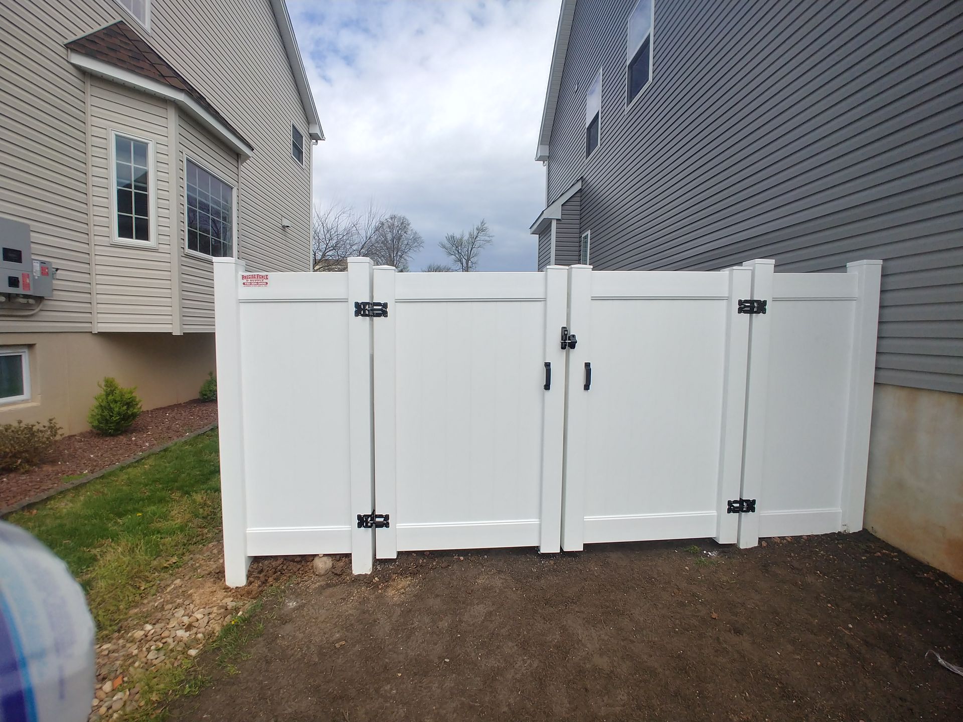 A white fence with two doors between two houses