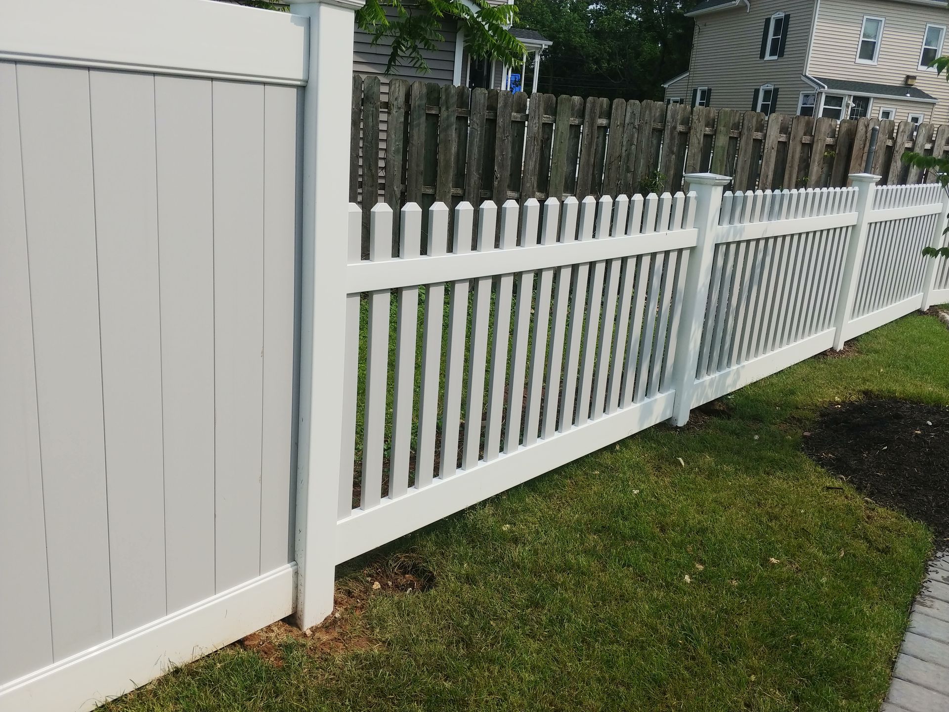 A white picket fence surrounds a lush green yard in front of a house.