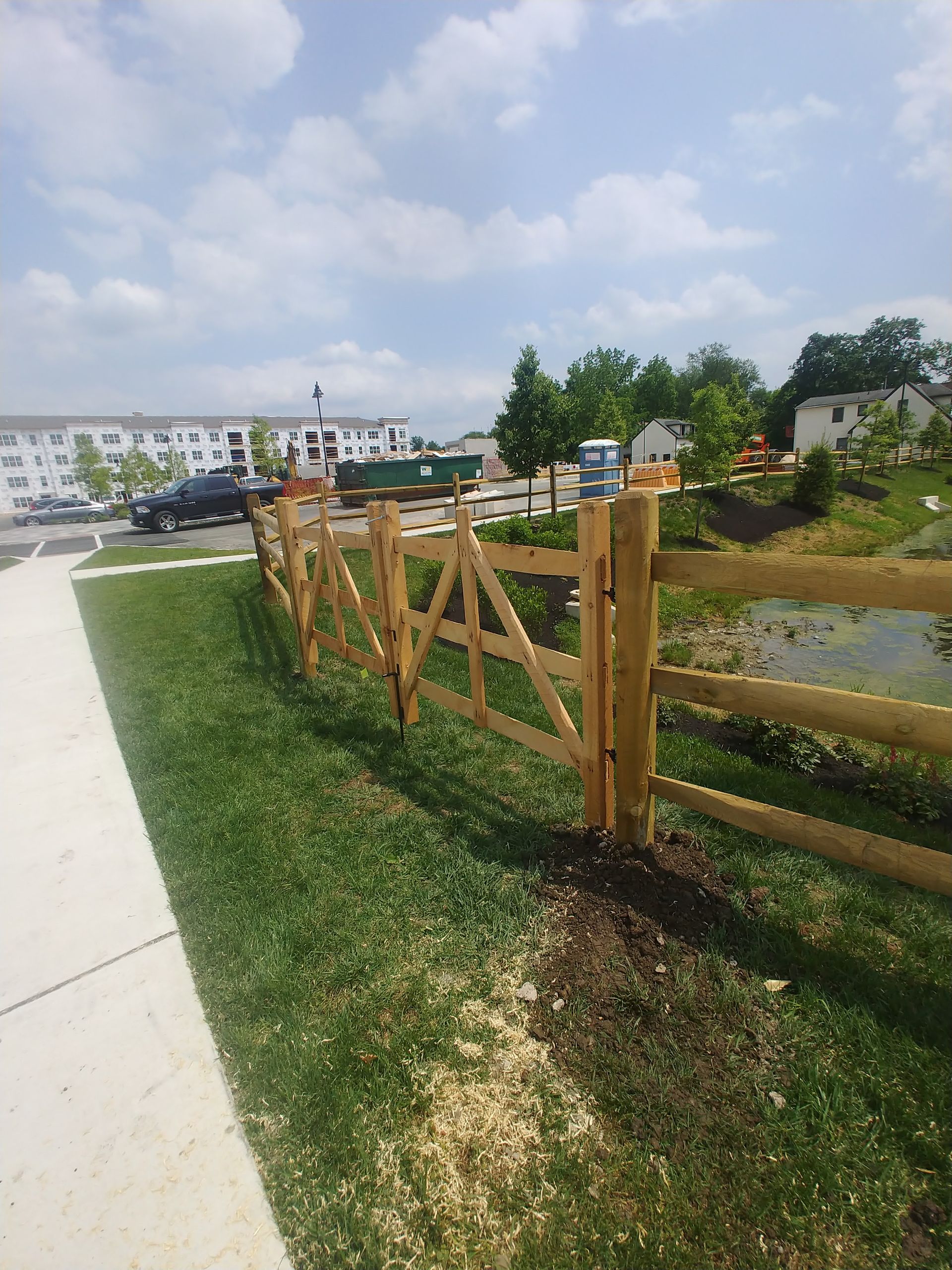 A wooden fence surrounds a grassy area next to a sidewalk.