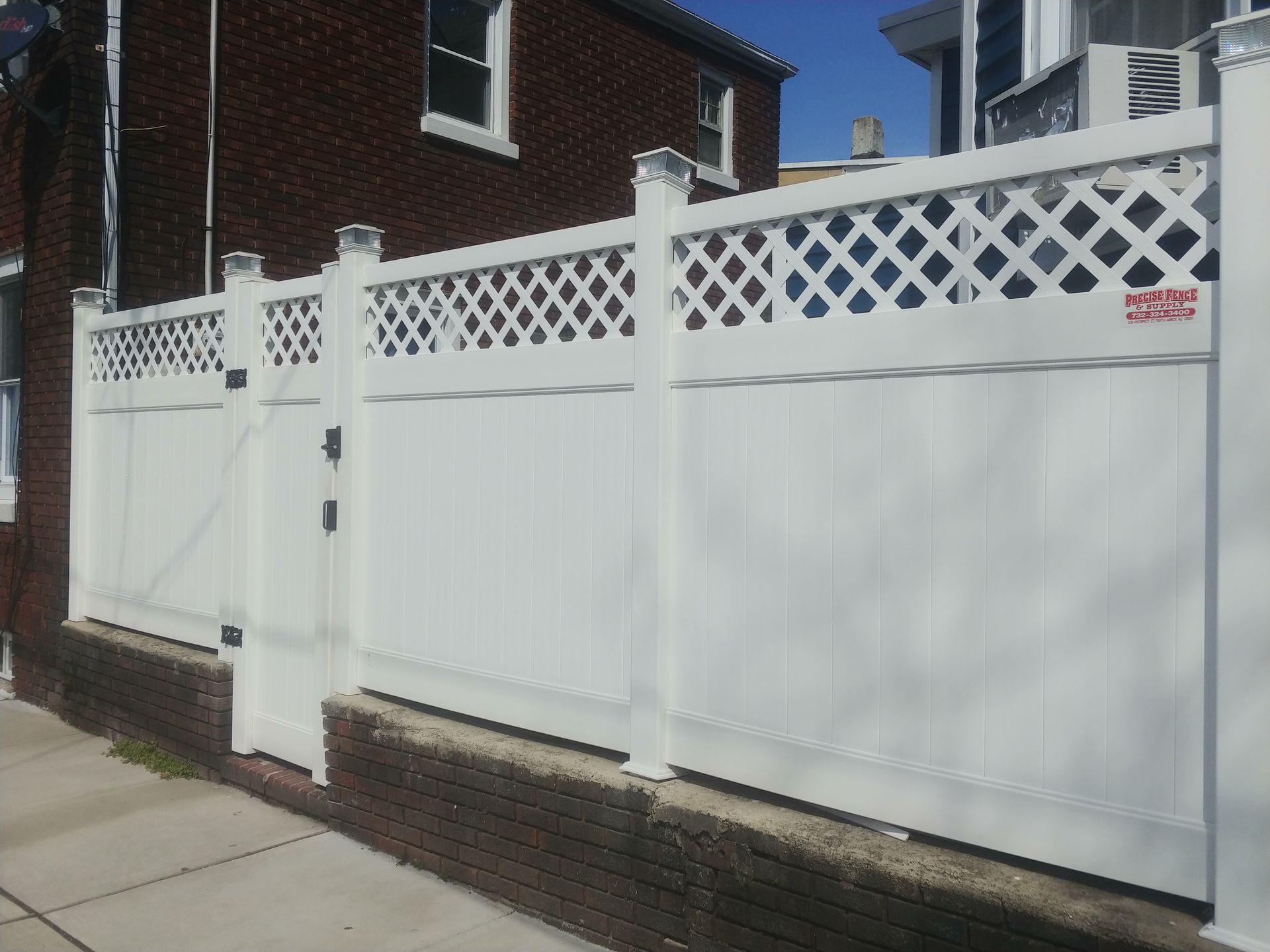 A white fence with a lattice design is next to a brick building