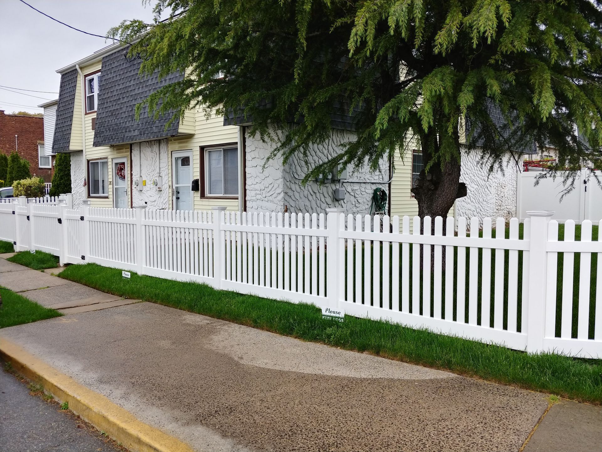 A white picket fence surrounds a house with a tree in front of it.