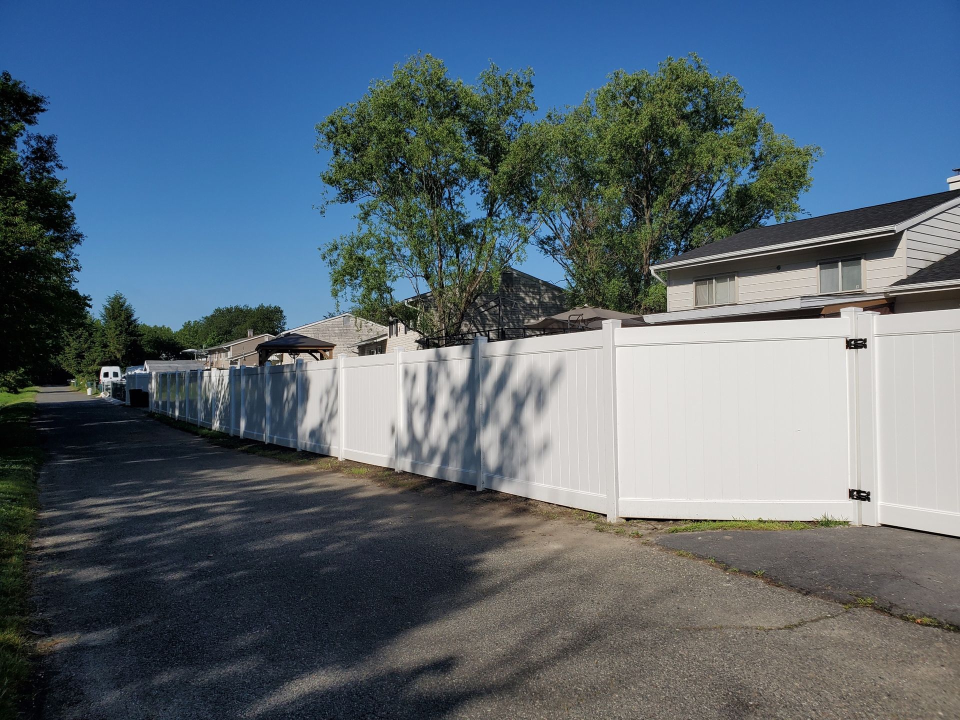 A white fence is along the side of a road next to a house.