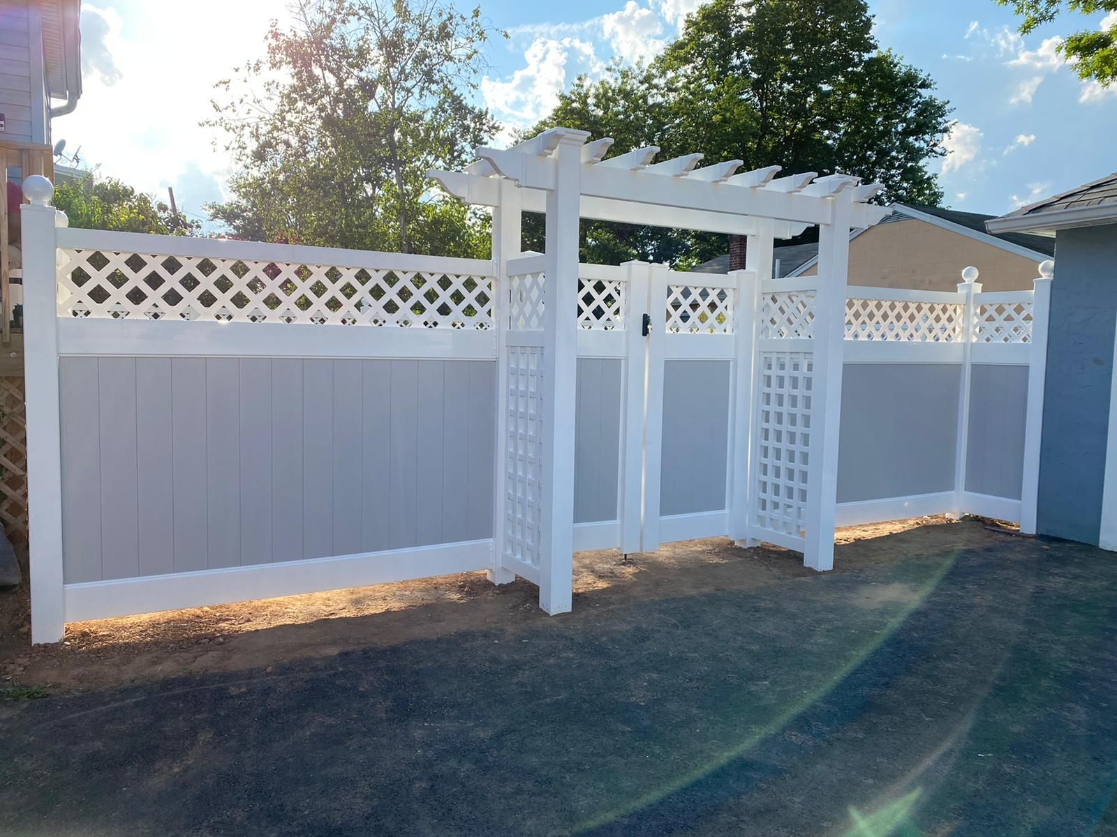 A white fence with a gate and a pergola in front of a house.