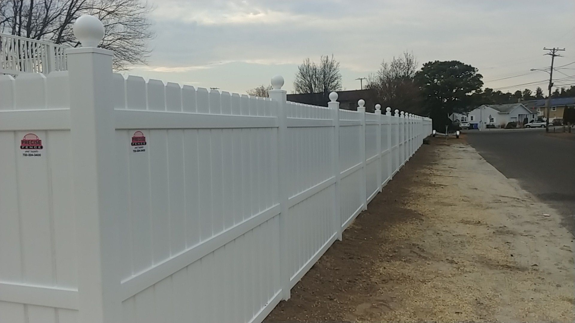 A long white fence is along the side of a road.