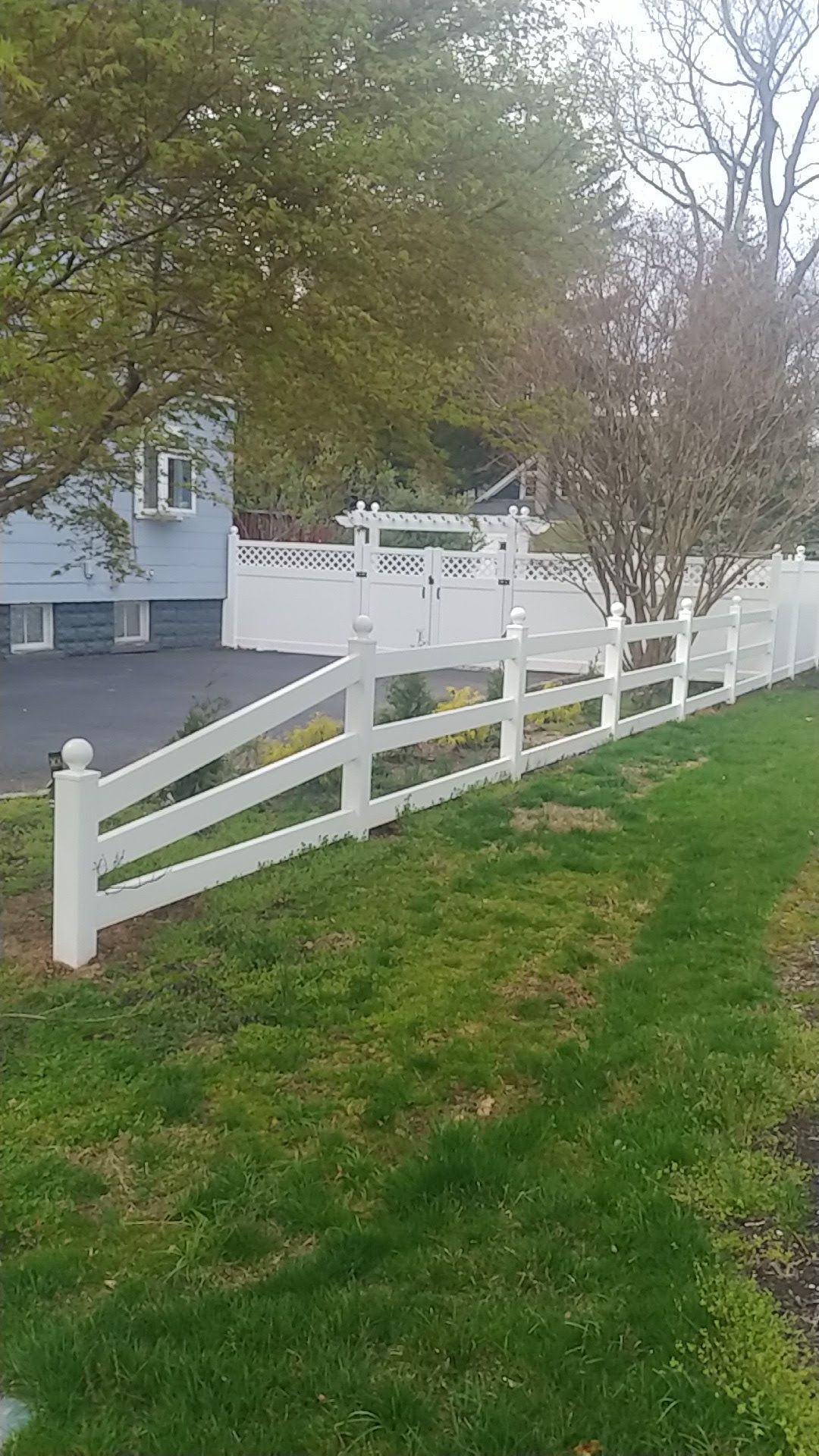 A white fence surrounds a lush green yard in front of a house.
