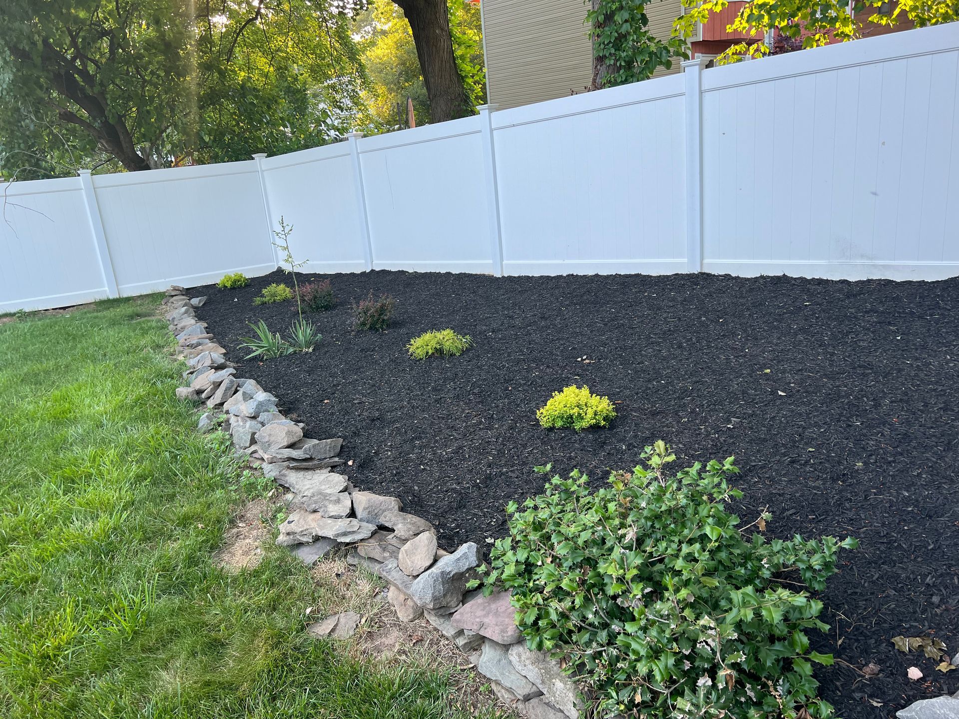 A white fence surrounds a garden with black mulch and rocks.