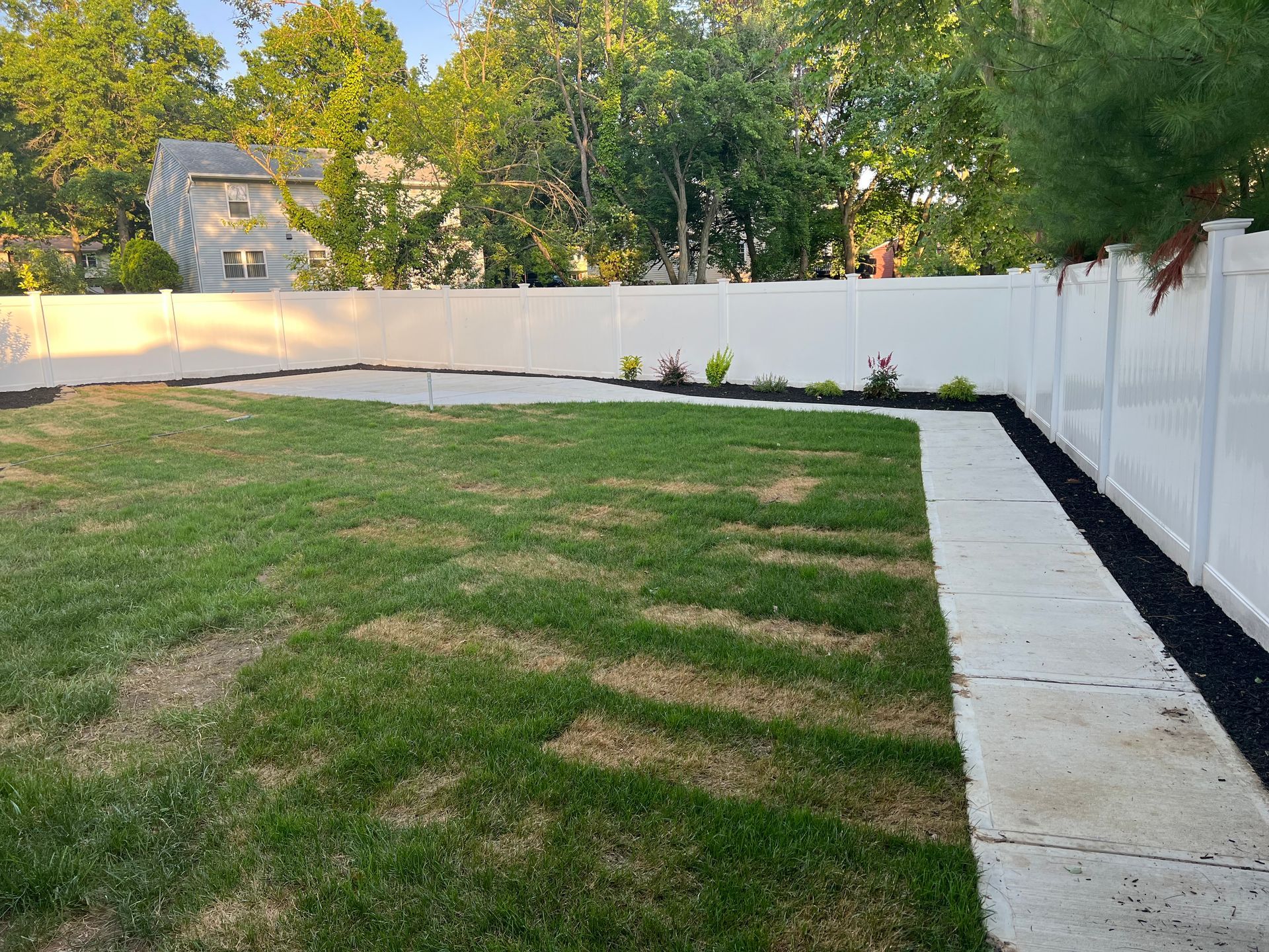 A backyard with a white fence and a lush green lawn.