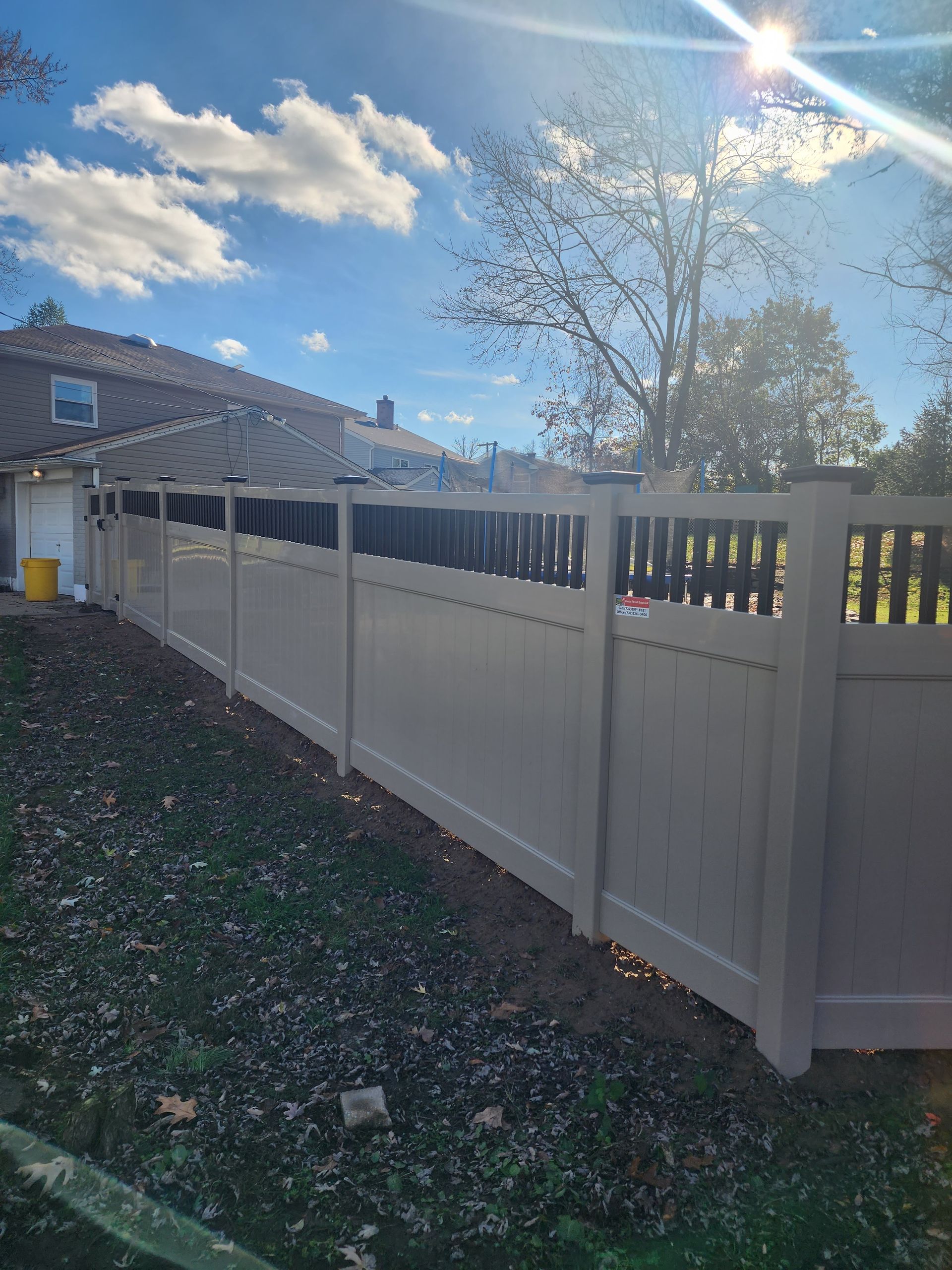 A white fence surrounds a backyard with a house in the background.