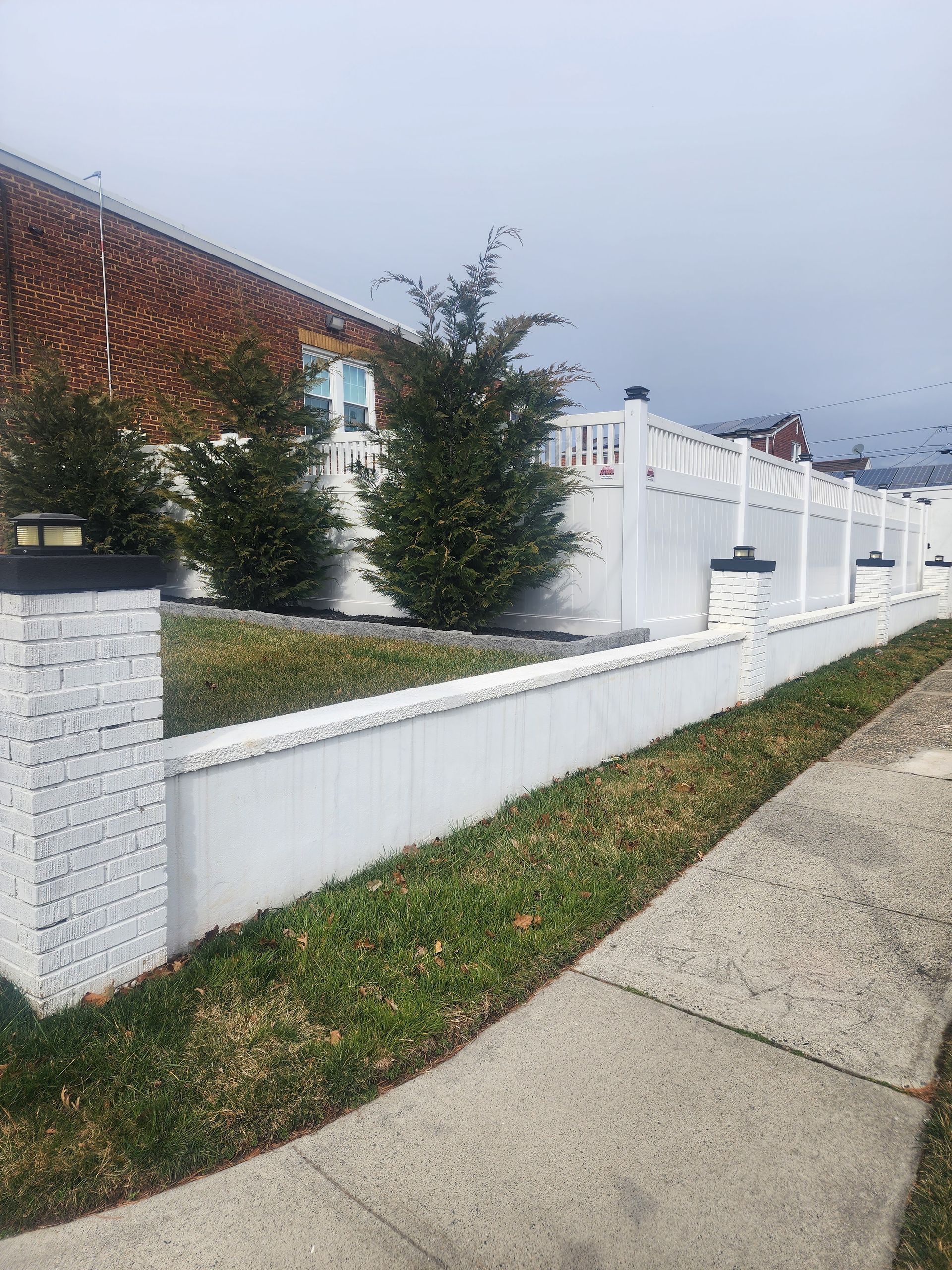 A white fence along a sidewalk in front of a house