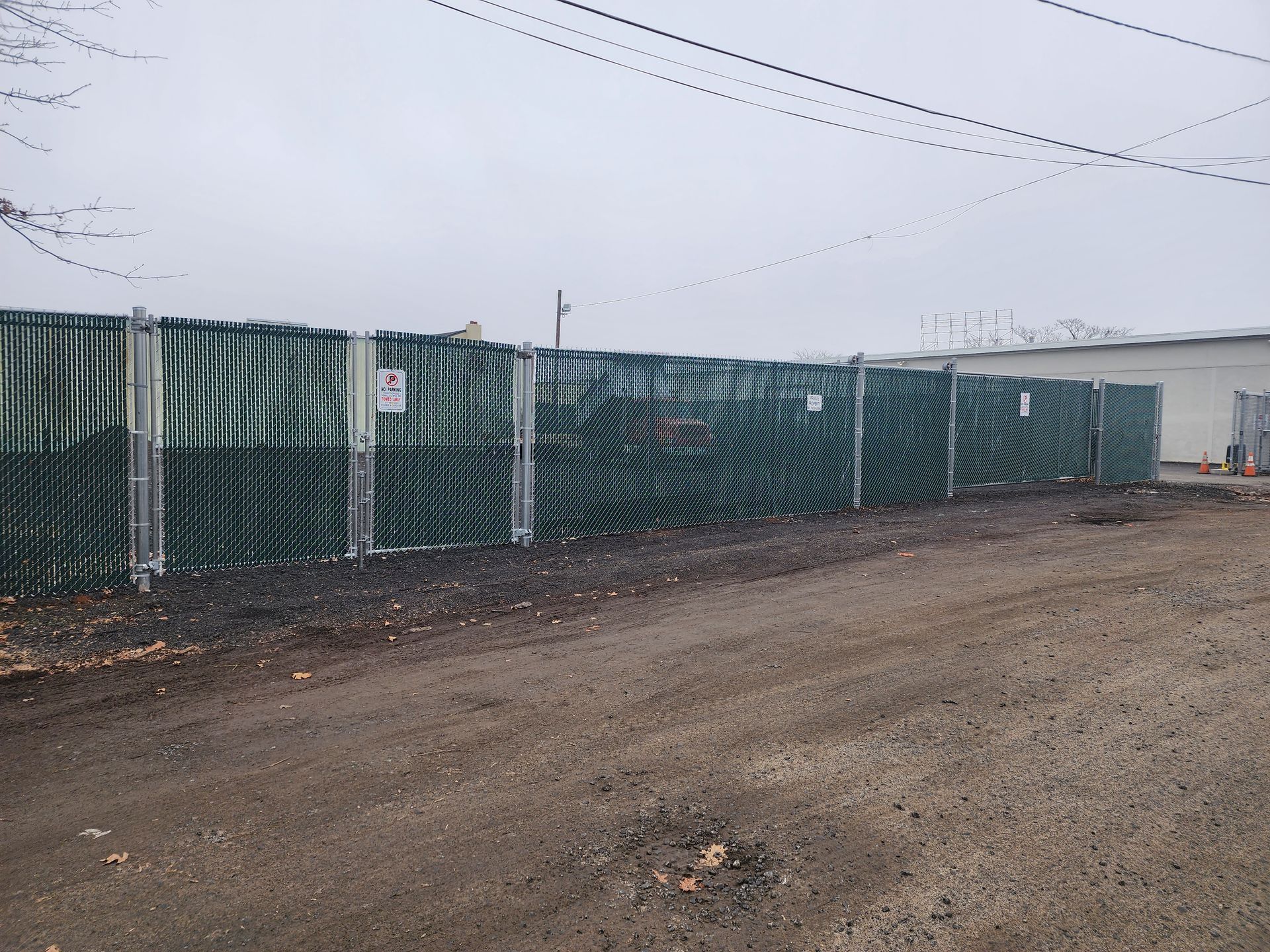 A fence is surrounding a dirt road with a building in the background.