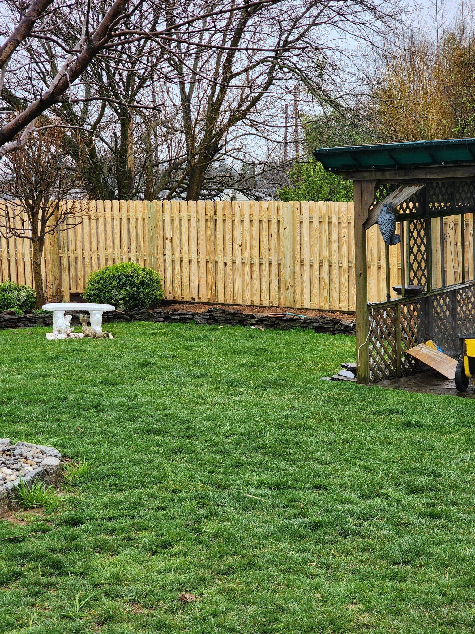 There is a wooden fence in the backyard with a gazebo and a picnic table.