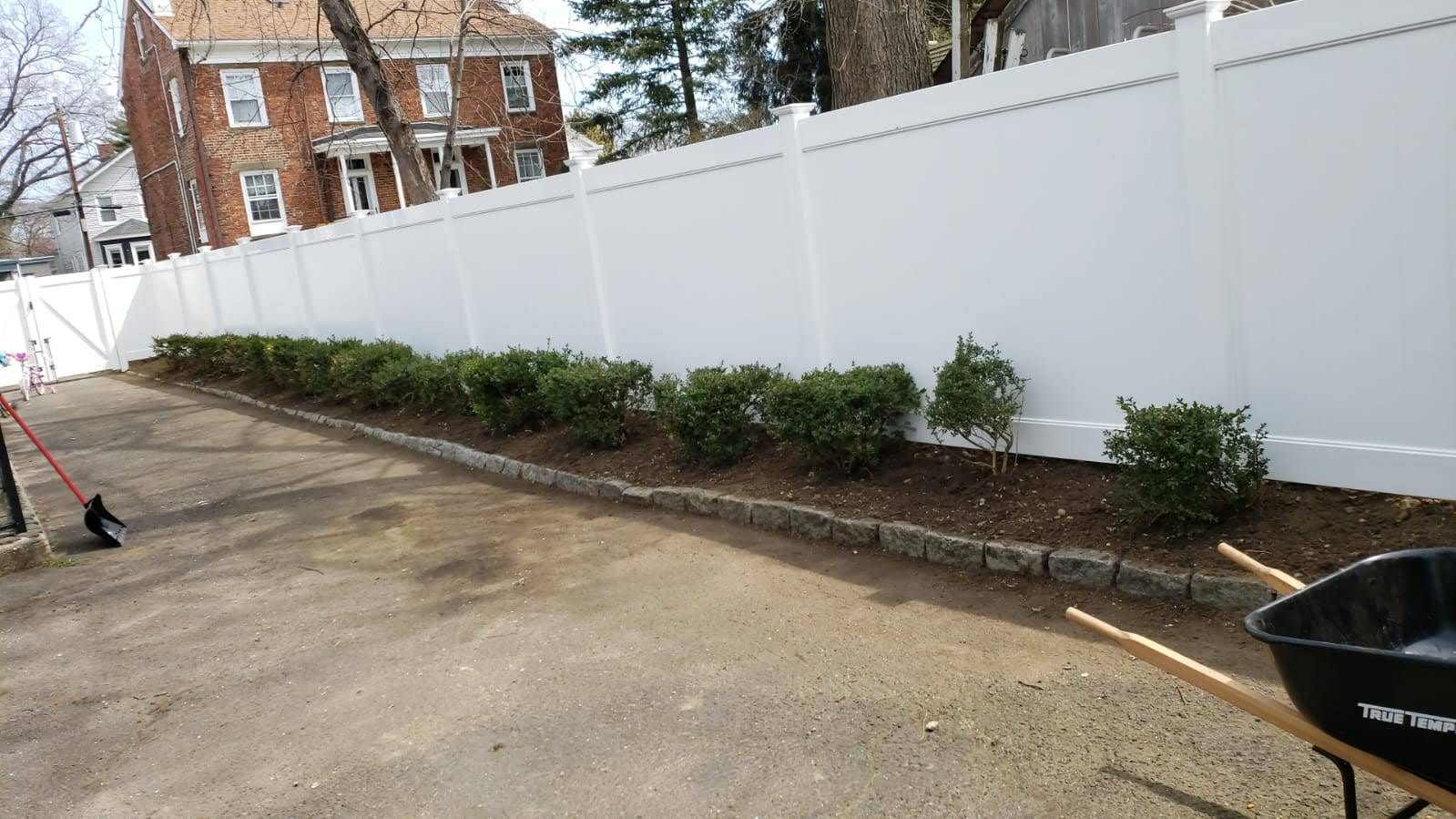 A white fence with a black wheelbarrow in front of it.