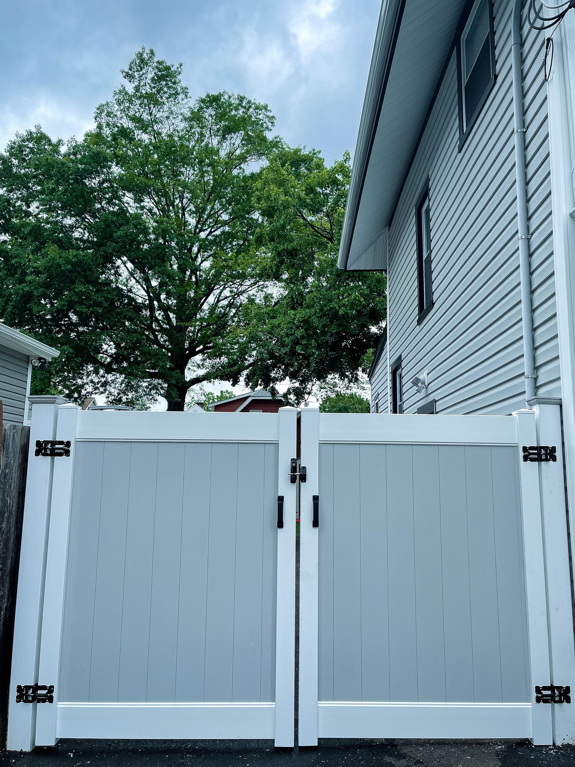 A white fence is sitting in front of a house with trees in the background.