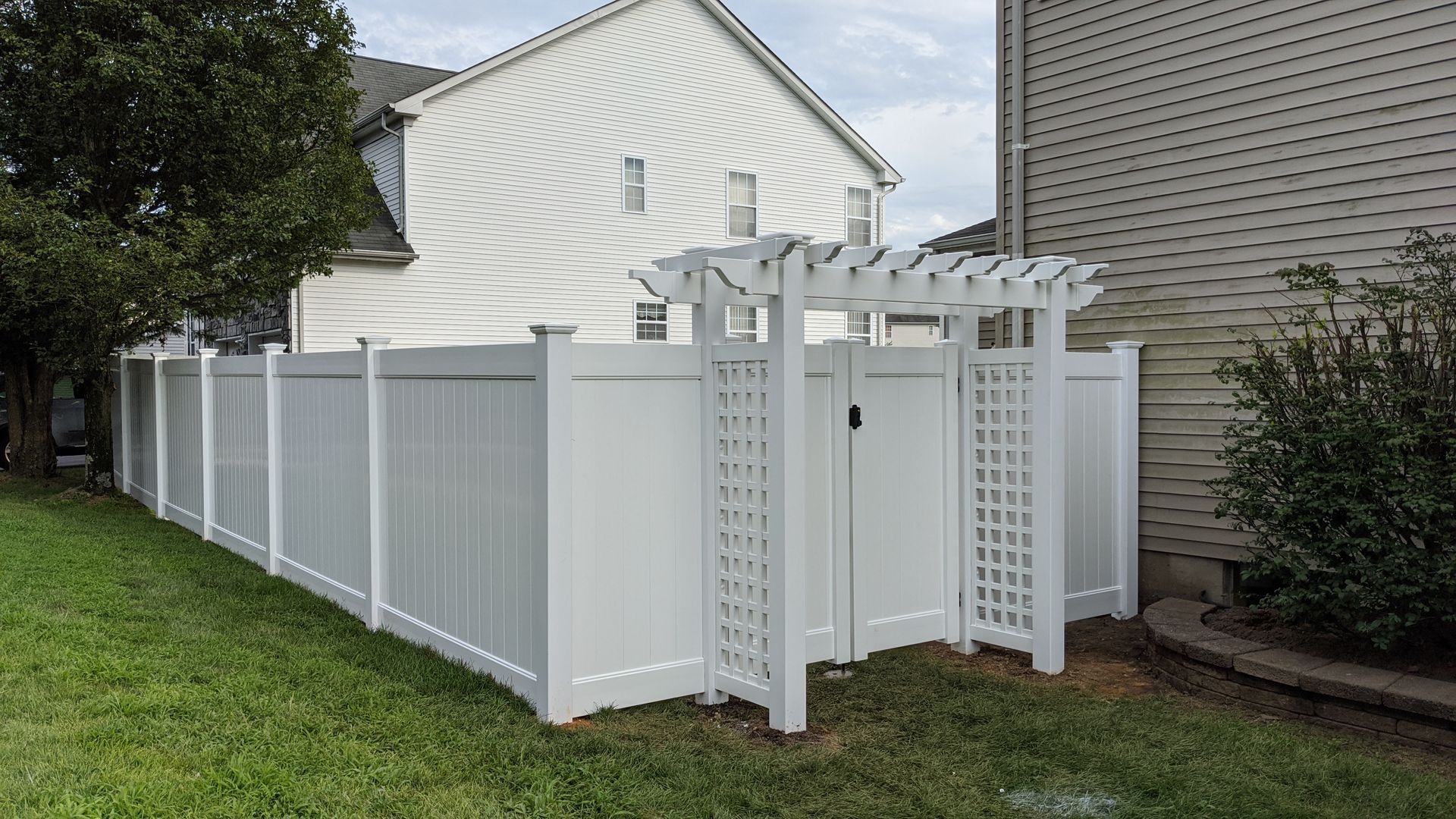 A white fence with a pergola in the backyard of a house.
