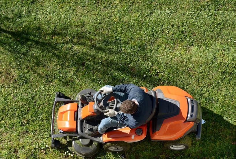 A Man is Riding a Lawn Mower on a Lush Green Lawn — Urunga Chainsaw and Mower in Urunga, NSW