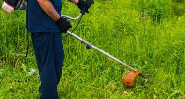 A Man is Using a Lawn Mower to Cut Grass in a Field — Urunga Chainsaw and Mower in Urunga, NSW