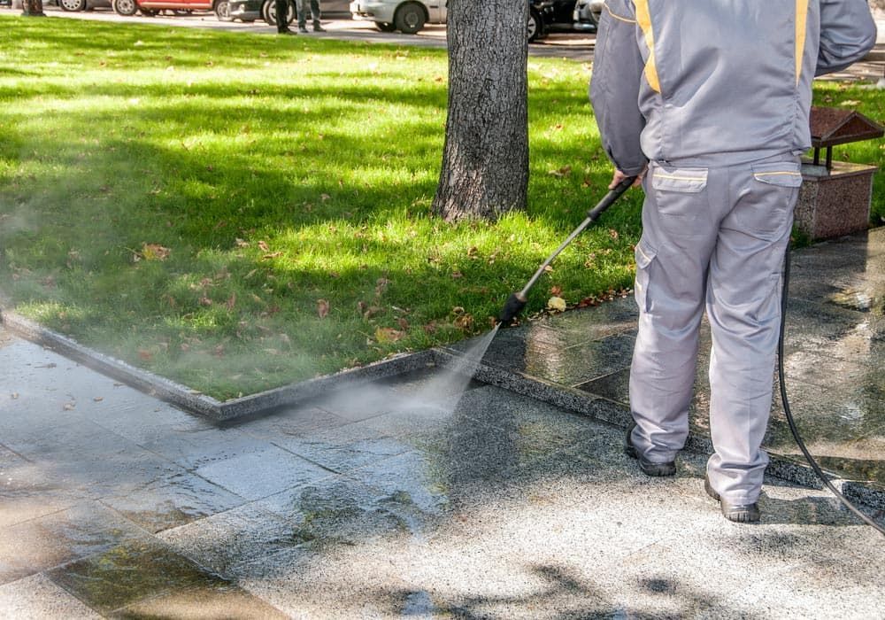 A Man is Using a High Pressure Washer to Clean a Sidewalk — Urunga Chainsaw and Mower in Urunga, NSW