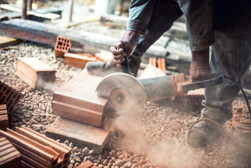A Man is Cutting Bricks With a Grinder on a Construction Site — Urunga Chainsaw and Mower in Urunga, NSW