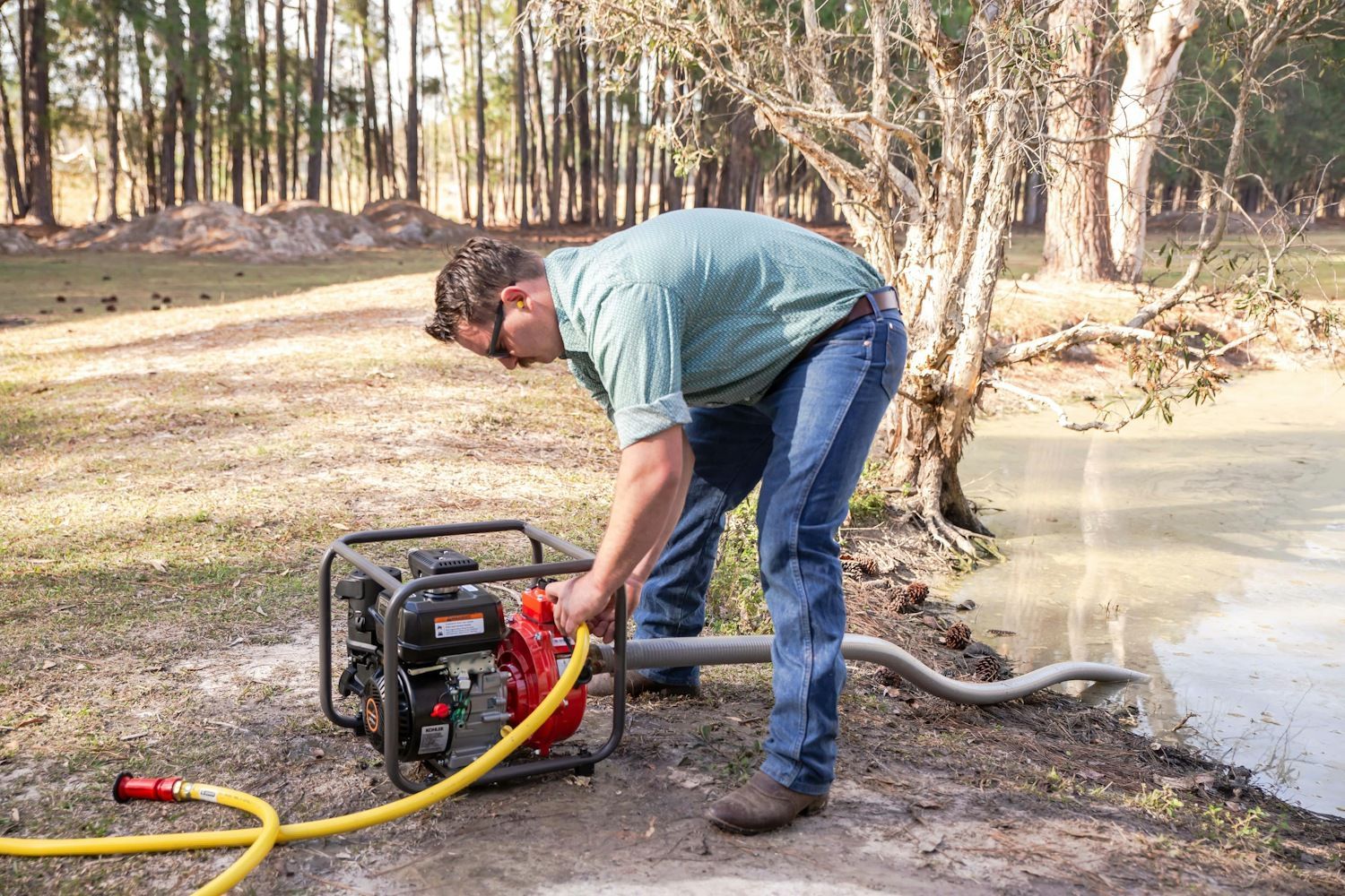 A Man is Pumping Water From a Generator Into a Pond — Urunga Chainsaw and Mower in Mid North Coast, NSW