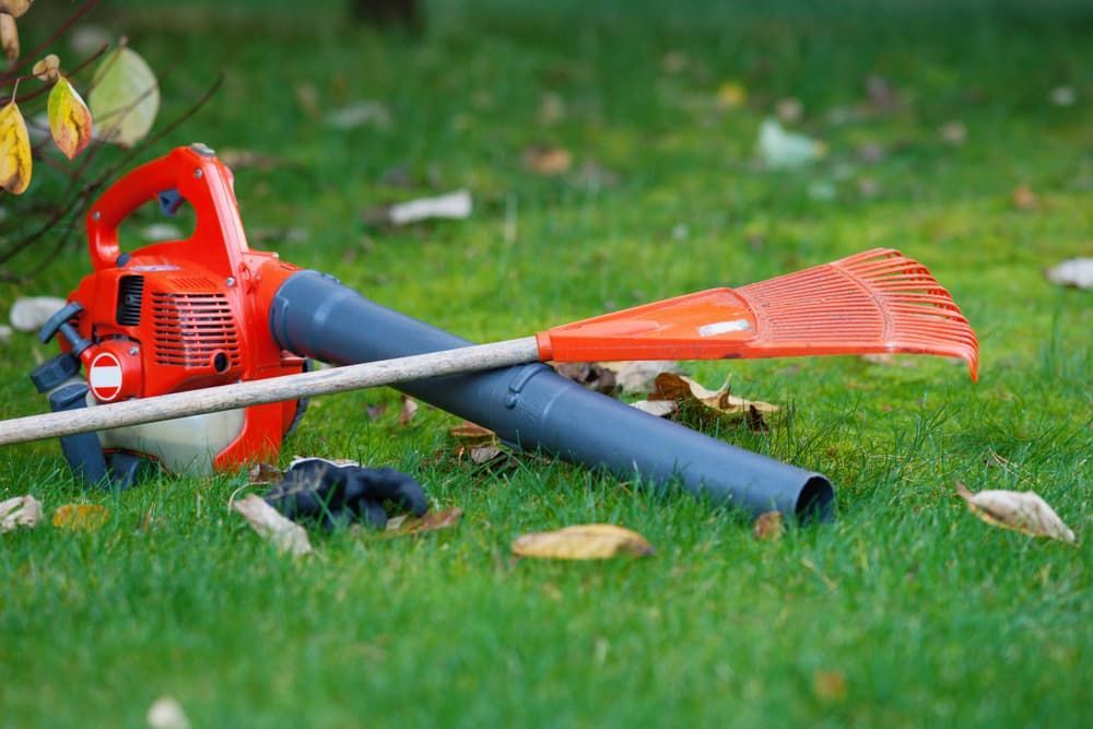 A Leaf Blower and Rake Are Laying on the Grass — Urunga Chainsaw and Mower in Urunga, NSW