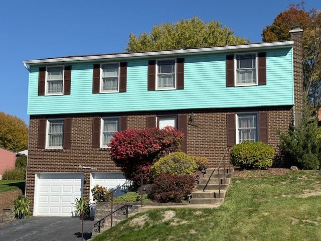A brick house with a green siding and brown shutters